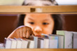 Asian little girl hand is finding and selecting a book on bookshelf in the library in vintage color tone