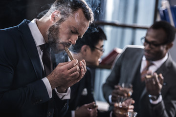 businessman smoking cigar with multicultural business team spending time behind