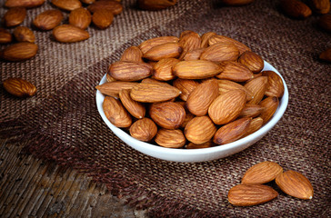 Wall Mural - Almonds in a bowl on textured wooden background. Organic food.