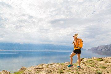 Wall Mural - Woman hiker with backpack, hiking at seaside and mountains