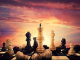 Fototapeta Tęcza - Successful boy standing on a chess piece meeting the sunrise on the horizon. Gigant chess figures scattered on the vintage chessboard. Symbol of business aspirations, freedom and leadership concept. 