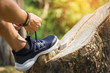 © snowing12 - Cropped shot of young man runner tightening running shoe laces, getting ready for jogging exercise outdoors. Male jogger lacing his sneakers standing on forest path before morning run