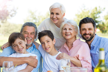 Family sitting at table outdoors, smiling
