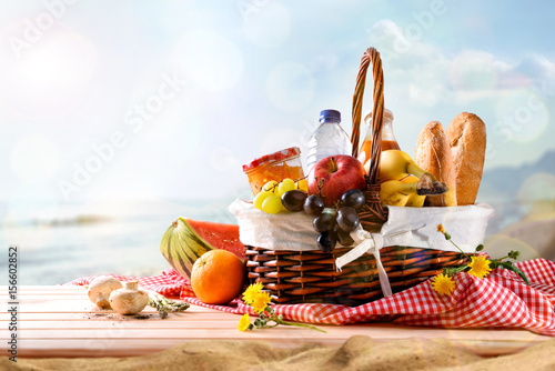 Zdjęcie XXL Pykniczny łozinowy kosz z jedzeniem na stole na plaży