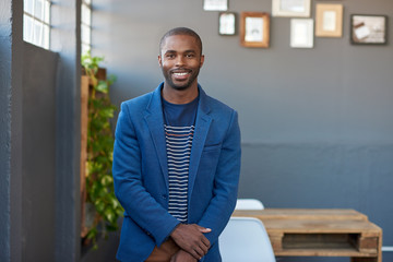 Wall Mural - Smiling young African businessman standing alone in an office