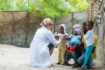 caucasian female doctor listening heart beat and breathing of little african girl , family looking m