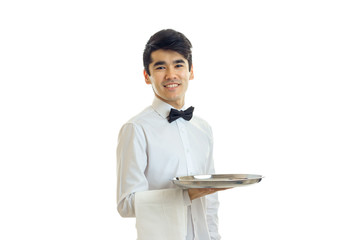 Wall Mural - attractive smiling young waiter looks at the camera and holding a tray with a towel