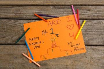 Overhead view of fathers day greeting card and crayons on table