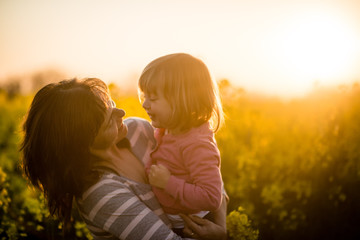 Wall Mural - Portrait of a smiling mother with baby girl at sunset background