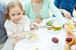 © pressmaster - Little girl eating flakes by dinner table with her family near by