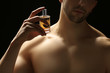© Africa Studio - Handsome man using perfume on black background