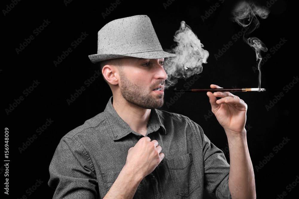 Handsome man smoking cigarette on dark background