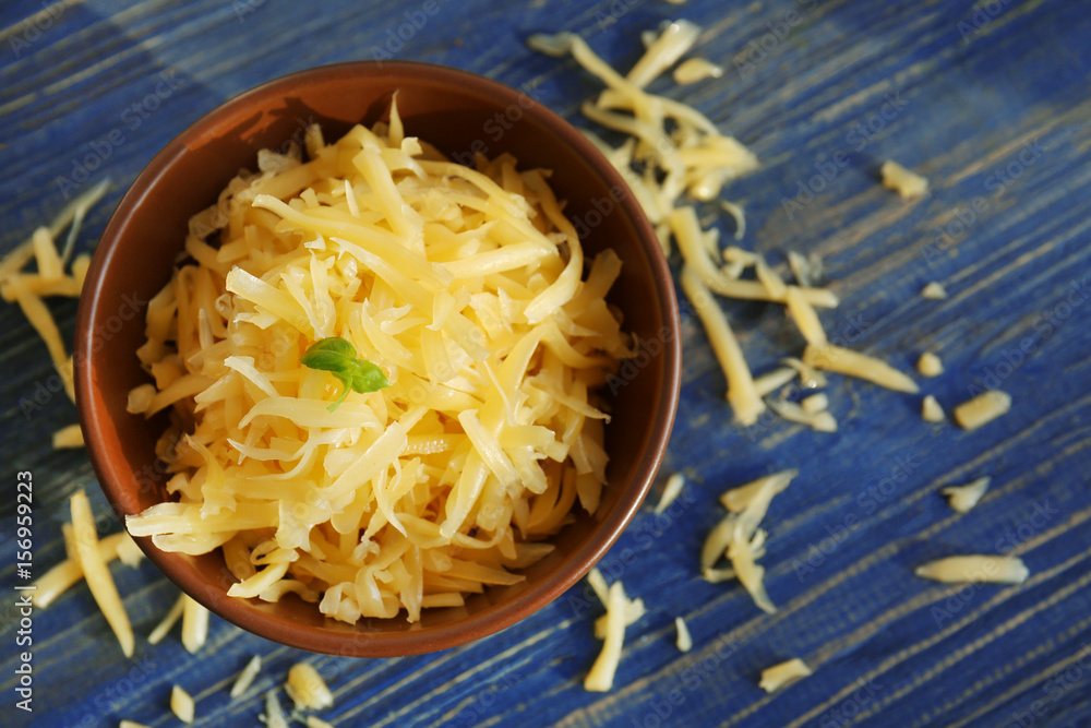 Bowl with grated cheese on wooden table