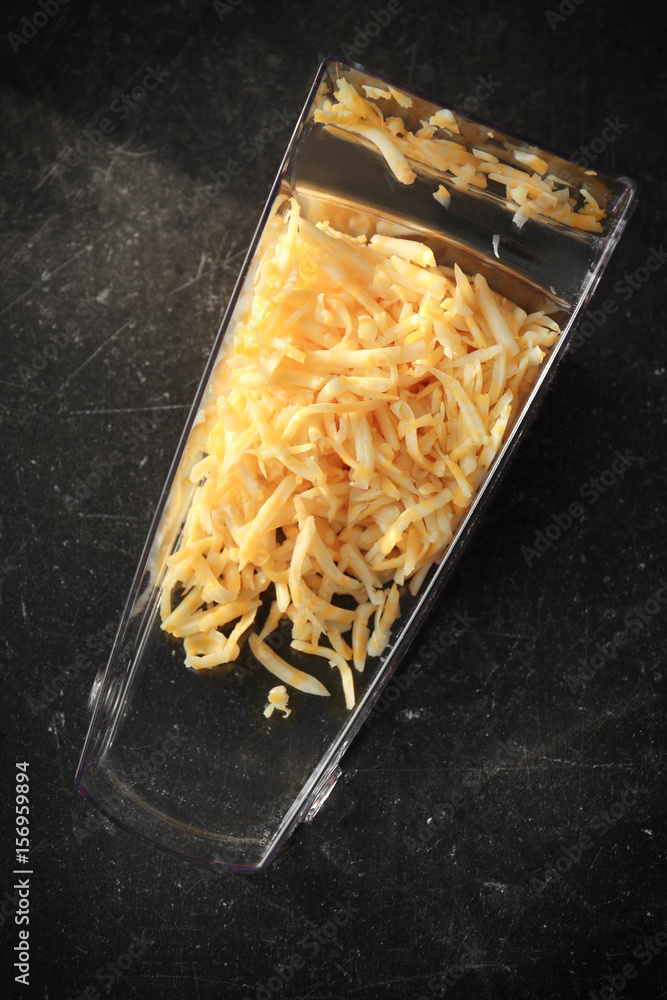 Plastic container with grated cheese on table