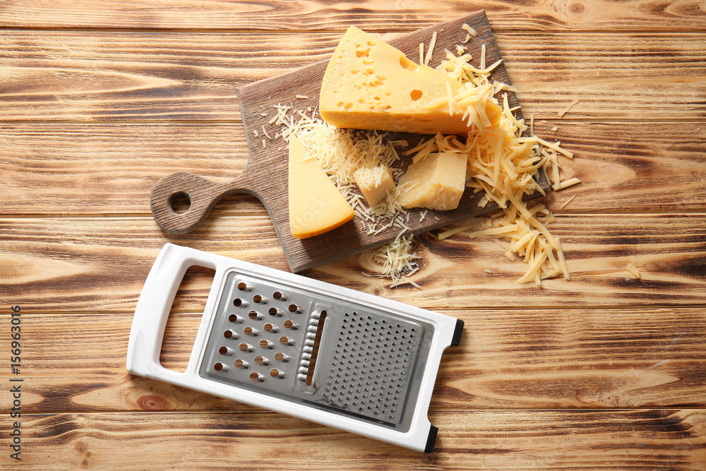 Grater and cutting board with cheese on wooden background