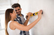 © didesign - Smiling young couple measuring wall with level tool, renovation concept