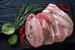 Top view of raw fresh pork loin steaks with seasonings on a black wooden background, horizontal shot