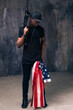 Afro american man in black cloth with flag and weapon stay on dark background. Gangster, patriotism, social problem, immigration, us citizenship, armed strike, bandit groups concept