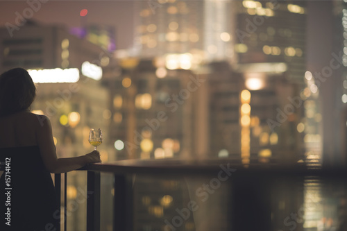 Beautiful young woman on the balcony in a black dress with a glass of wine on th Poster