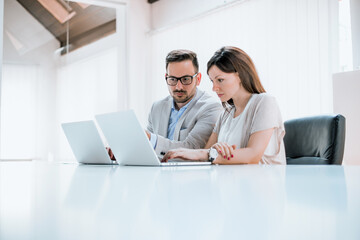 Business man and woman colleagues sitting with laptops on desk in office