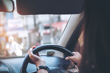 Woman Holding On Black Steering Wheel While Driving A Car With Traffic Background