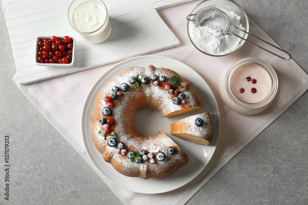 White plate with delicious sliced dessert and ingredients for yogurt cake on grey table