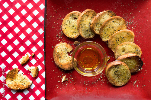 Fotografia, Obraz french bread slices with olive oil on red plate and checkerboard tablecloth