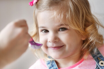 Poster - Mother feeding cute little girl with yogurt at home, closeup