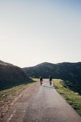 Two professional road cyclist team mates athletes ride their bikes into far away diatnce on empty mountain road