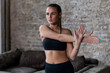 © undrey - Fit young woman in sportswear doing shoulder and arm stretching exercise before workout indoors in loft apartment