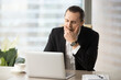 © fizkes - Man yawning while sitting at desk in front of laptop. Businessman struggling with drowsiness at workplace. Entrepreneur feeling severe lack of sleep, fatigue because of after-hour work. Overworking
