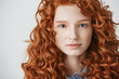Close up of beautiful girl with curly red hair and freckles looking at camera over white background.