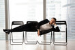 © fizkes - Bored attractive man in stylish business suit lying relaxed on office chairs in a row, resume in hand. Job applicant tired of long waiting for his turn on interview. Post candidate in reception room