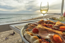 Homemade Pizza With Ham Tomato Olives And Peppers With Glass Of White Wine And The Beach At Sunset In Background