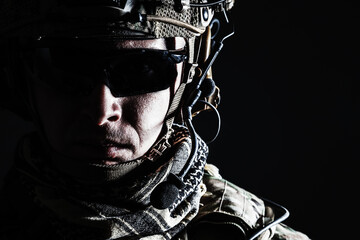 Elite member of US Army rangers in combat helmet and dark glasses. Studio shot, dark black background, looking at camera, dark contrast