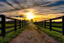 Dirt Road Leading To A Barn With Sunset In Background