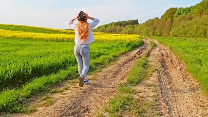 Wall Mural - Woman with long hair walks on path near green field during summer afternoon