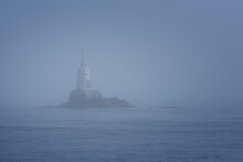 Lighthouse Along Rocky Coastline On Foggy Morning
