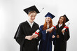 © Cookie Studio - Happy international graduates smiling rejoicing holding diplomas over white background.