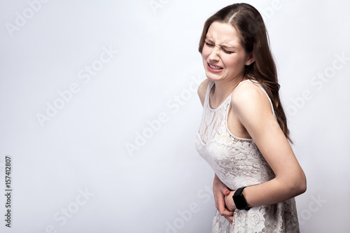 Fényképezés Portrait of beautiful woman with freckles and white dress and smart watch with stomach pain on silver gray background