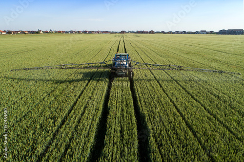 Cuadros en Lienzo Tractor sprinkling pesticides against bugs on agricultural - Aerial view taken b