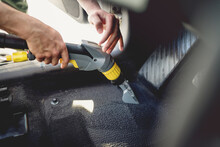 Professional detailer vacuuming carpet of car interior, using steam vacuum