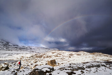 Poster - A rainbow over a hiker on a snow covered Beinn Eighe in the Scottish Highlands, Scotland, UK.