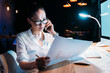 © LIGHTFIELD STUDIOS - Young asian businesswoman in eyeglasses holding blueprint and talking on smartphone