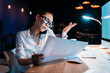 © LIGHTFIELD STUDIOS - Young asian businesswoman in eyeglasses holding blueprint and talking on smartphone