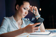 © LIGHTFIELD STUDIOS - pensive tired asian businesswoman holding eyeglasses and using smartphone, working late at the office
