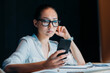 © LIGHTFIELD STUDIOS - young tired asian businesswoman in eyeglasses using smartphone and working till late in office
