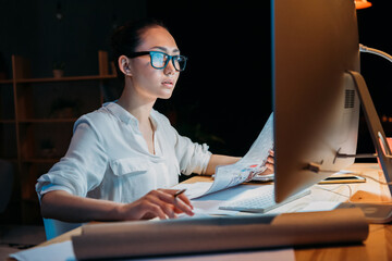 young concentrated asian businesswoman in eyeglasses working with documents and computer
