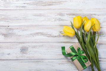 Wall Mural - bouquet of yellow tulips and a gift with a yellow ribbon on a wooden background