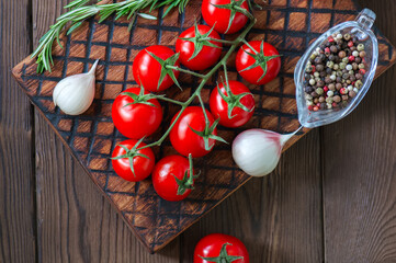 Fresh raw cherry tomatoes on a wooden board with pepper garlic and rosemary bunch. Close up and copy space. Top view.